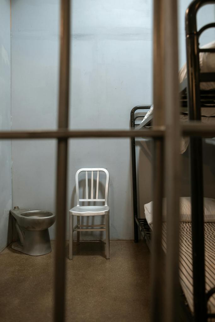 Prison Cell with a metal chair, a metal toilet, and bunk beds behind bars